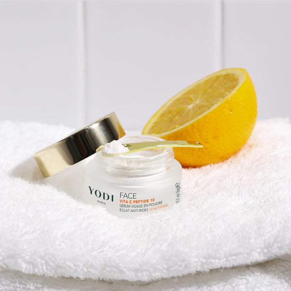 Sérum poudre Éclat & Anti-rides Vita C Peptide 10 Yodi, pot ouvert à côté d'un demi-citron