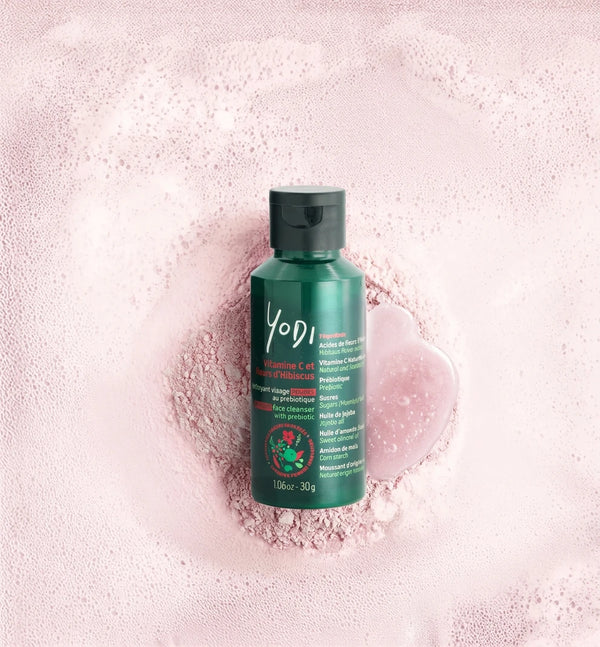 Nettoyant visage en poudre Éclat & Douceur Yodi à la vitamine C et à l'hibiscus, posé sur sa poudre rose