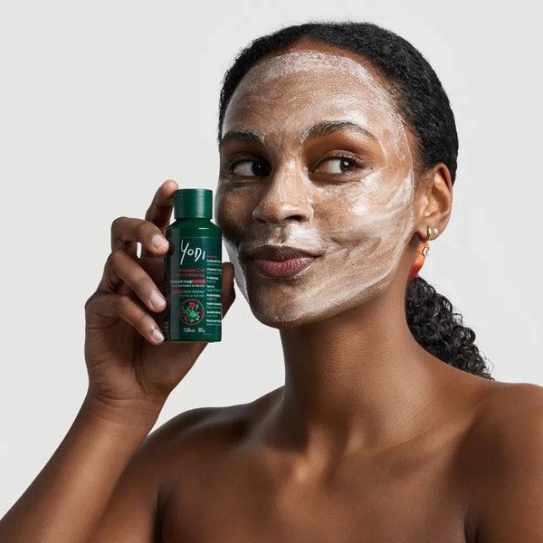 Femme au visage recouvert du lait nettoyant Éclat & Douceur Yodi, flacon en main